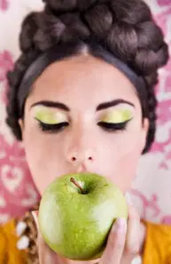 Beautiful white woman eating a granny smith apply with eyes closed to show her granny green apple eyeshadow colored eyelids with hair braided into a bun that sits on top of head. Absolutely gorgeous pictures